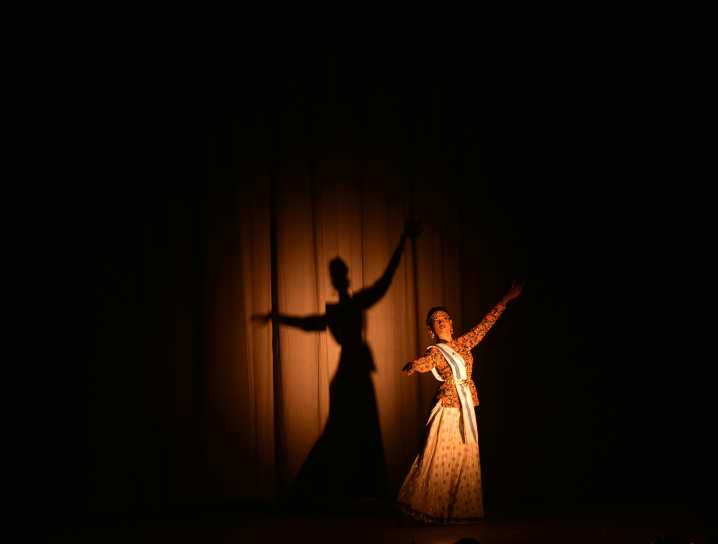 Solo theatrical actress with arms dramatically outstretched in the spotlight.